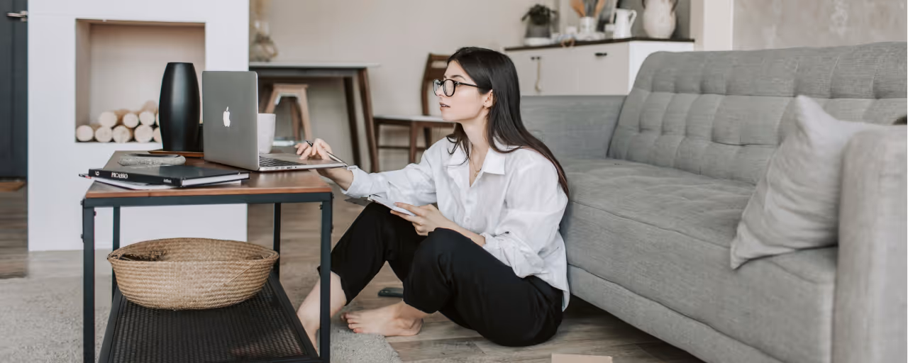 A remote worker sitting on the floor at home looking at her laptop